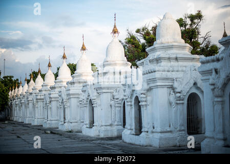 MANDALAY, Myanmar – Reihen von unberührten weißen Kyauksa gu (Höhlen mit Steininschriften) erstrecken sich über das Gelände der Kuthodaw-Pagode. Der 1857 von König Mindon erbaute Komplex enthält 729 Marmorplatten, die zusammen das als das größte Buch der Welt bekannt ist. Jede kleine Stupa beherbergt eine Marmortafel auf beiden Seiten mit Text aus dem Tipitaka, dem vollständigen Pali-Kanon des Theravada-Buddhismus. Die geordnete Anordnung dieser Strukturen spiegelt traditionelle buddhistische Architekturprinzipien wider. Stockfoto