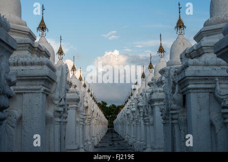 MANDALAY, Myanmar – Reihen von unberührten weißen Kyauksa gu (Höhlen mit Steininschriften) erstrecken sich über das Gelände der Kuthodaw-Pagode. Der 1857 von König Mindon erbaute Komplex enthält 729 Marmorplatten, die zusammen das als das größte Buch der Welt bekannt ist. Jede kleine Stupa beherbergt eine Marmortafel auf beiden Seiten mit Text aus dem Tipitaka, dem vollständigen Pali-Kanon des Theravada-Buddhismus. Die geordnete Anordnung dieser Strukturen spiegelt traditionelle buddhistische Architekturprinzipien wider. Stockfoto