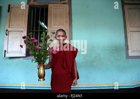 Junger buddhistischer Mönch mit Blumen im Kloster in Amarapura, Myanmar Stockfoto