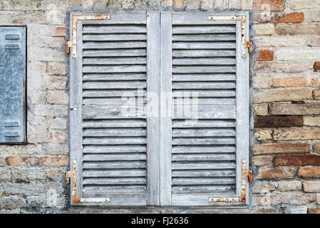 Alte Fenster mit weißen geschlossenen Fensterläden aus Holz in Ziegelmauer Hintergrundtextur Foto Stockfoto