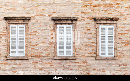 Drei Fenster mit weißen geschlossenen Fensterläden aus Holz in alten Ziegelmauer Hintergrundtextur Foto Stockfoto