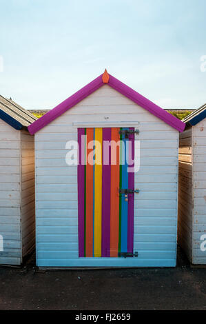 Eine Strandhütte in einer Reihe von Hütten erhellt schattige Position mit einer Tür lackiert in brilliant farbigen Streifen im Goodrington Sands Stockfoto