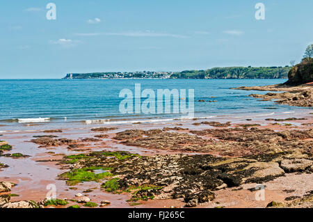 Felsen, durch die rötlich gefärbten Sand Kontrast stark mit dem Blau des Meeres, die Himmel und die grüne Vegetation auf der Landzunge Stockfoto