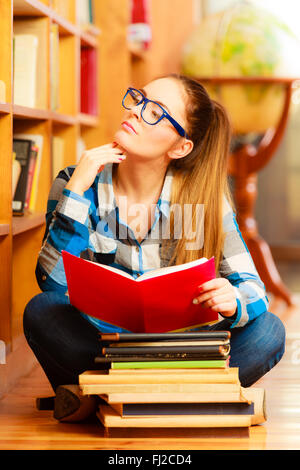 Bildungskonzept der Schule. Clevere Studentin Langhaar Mädchen Blau Brille sitzen am Boden im College-Bibliothek mit Stapel Bücher Stockfoto