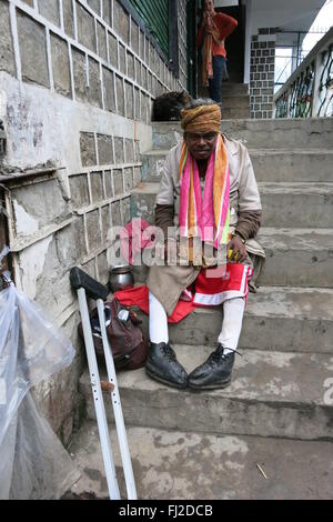 Würdige verkrüppelten Bettler sitzt auf Schritte mit Krücke und Almosen in Metall-Topf in McLeod Ganj Indien akzeptiert Stockfoto