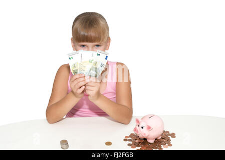 Mädchen, die Geld in den Händen halten und haben ein Sparschwein auf dem Tisch, isoliert Stockfoto
