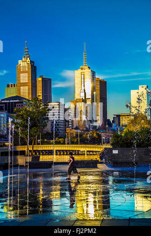 Kind spielt in Brunnen Southbank gegen Wolkenkratzer am späten Nachmittag leichte in Stadt Melbourne Australien Stockfoto