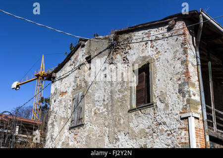 Großes altes verlassenes Haus mit faulen Fenstern in Renovierung. Eine gelbe Kran im Hintergrund. Stockfoto