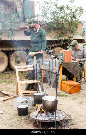 Zweiten Weltkrieg Re-enactment. Deutschen Feldlager, Tiger Tank im Hintergrund, Soldat an Radio Sitzen und einem anderen zu Fuß, mit Gewehr und Panzerfaust. Stockfoto