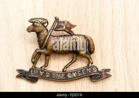 Ersten Weltkrieg, der Große Krieg. British Army Cap Badge auf holzmaserung Hintergrund. 1. freiwilligen Bataillon der Queen's Regiment. Eine ram-holding Flag. Stockfoto