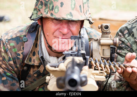 Zweiten Weltkrieg Re-enactment. Waffen-SS-Mann in der Tarnung einheitliche, hinter einem Maschinengewehr mit Barrel auf Viewer, Auge - Kontakt. Close-up. Stockfoto