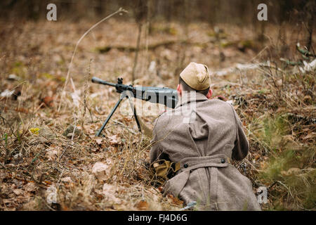 Nicht identifizierte Re-Enactor gekleidet als Zweiter Weltkrieg sowjetische russischer Soldat mit Maschinengewehr im Waldboden versteckt. Stockfoto