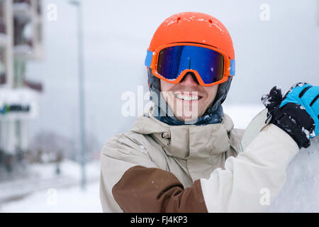 Mann-Snowboarder tragen orange Helm, graue Jacke, schwarze und blaue Handschuhe stehend mit snowboard Stockfoto