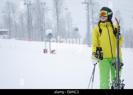 Skifahrerin stehend mit Skiern in der einen Hand auf Hintergrund herrlicher Berglandschaft Stockfoto