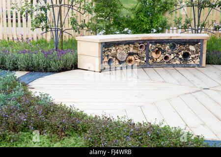 Kleiner, wildtierfreundlicher Garten mit kreisförmiger Holzterrasse mit Terrasse und Bank und Insektenhotel Motel UK Stockfoto