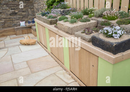 Kleiner städtischer Garten Steinplatten Terrasse Aufbewahrungsschränke eine Ausstellung von alpinen Pflanzen in Steintrog Container Container - Sitzbereich Steinbank UK Stockfoto