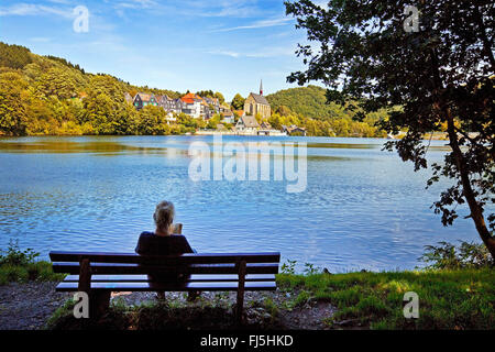 Frau sitzt auf einer Bank am Seeufer der Stausee Beyenburg, Altstadt von Beyenburg und Kloster Kirche St. Maria Magdalena im Hintergrund, Wuppertal, Bergisches Land, Nordrhein-Westfalen, Deutschland Stockfoto