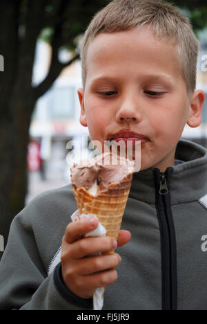 kleiner Junge mit verschmierten Gesicht Essen mit Freude ein Schokoladeneis, Porträt eines Kindes, Deutschland Stockfoto