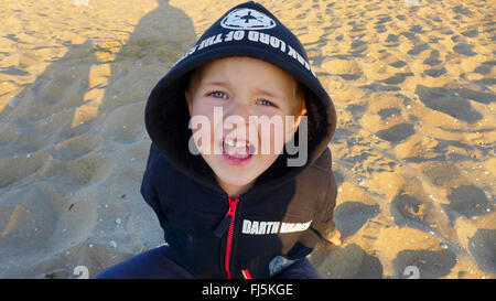 kleiner Junge kauert auf dem Sandstrand, Niederlande