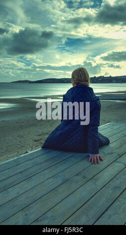 junge Frau sitzt auf Holz am Strand Stockfoto