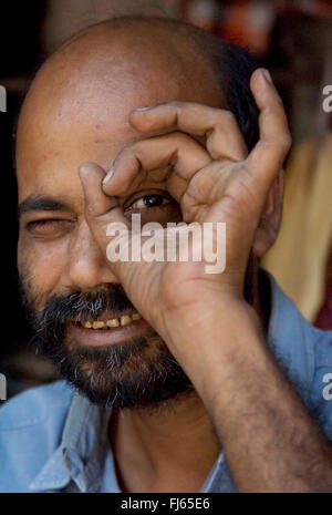 Mann, spähen durch ein Loch gebildet mit seinem Daumen und Zeigefinger, Indien, Varanasi Stockfoto