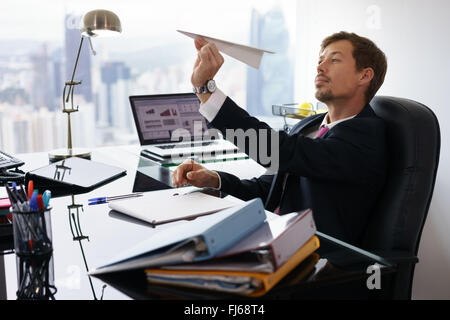 Corporate Manager in modernen Büro nimmt sich eine Auszeit und bereitet einen Papierflieger. Die gelangweilten Mann träumt von seinen nächsten Urlaub Stockfoto