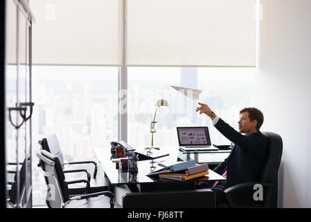 Corporate Manager in modernen Büro nimmt sich eine Auszeit und bereitet einen Papierflieger. Die langweilig Mann träumt von seinem nächsten Urlaub und l Stockfoto