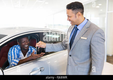 Autoverkäufer Übergabe neuer Autoschlüssel an Kunden sitzen im Fahrzeug im showroom Stockfoto