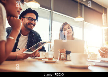 Porträt von glücklicher junger Mann sitzen und reden mit Freunden in einem Café. Junge Menschen in einem Coffee-Shop mit digital-Tablette und la Stockfoto