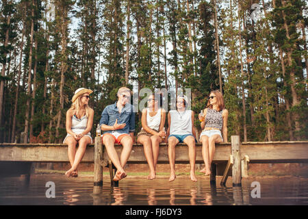 Porträt der jungen Freunde am Steg sitzen und reden. Junge Männer und Frauen, die einen Tag am See zu genießen. Stockfoto