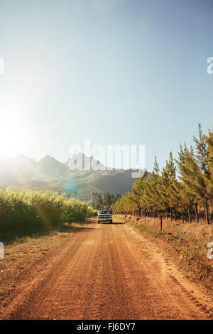 Outdoor-Bild von weit entfernten Auto nähert sich auf einem ländlichen Feldweg an einem sonnigen Tag. Auto über die Landstraße fahren. Stockfoto