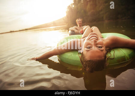 Porträt der glückliche junge Frau mit ihrem Freund im Hintergrund am See in einer Innertube schweben. Junges Paar in See auf inf Stockfoto