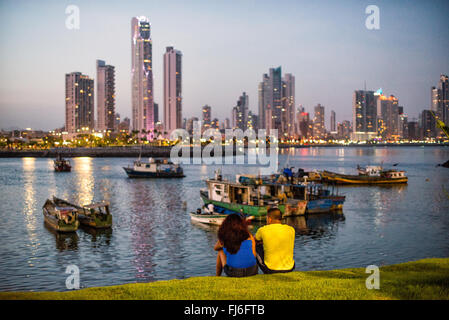 PANAMA-STADT, Panama — Ein Paar genießt an einem Sommerabend die Aussicht in Panama-Stadt, Panama, mit den modernen Wolkenkratzern von Punta Paitilla, die im Hintergrund eine Stadtlandschaft bilden, mit den traditionellen Holzfischbooten von Panama-Stadt im Vordergrund. Am Ufer von Panama City, Panama, an der Panama Bay. Stockfoto