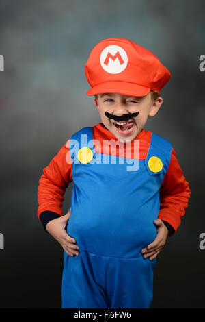 Junge verkleidete sich als Super Mario Bros vor grauem Hintergrund. Stockfoto