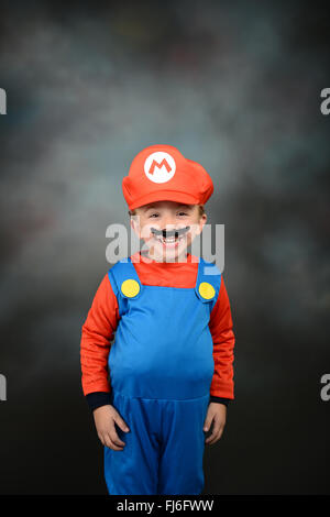 Junge verkleidete sich als Super Mario Bros vor grauem Hintergrund. Stockfoto