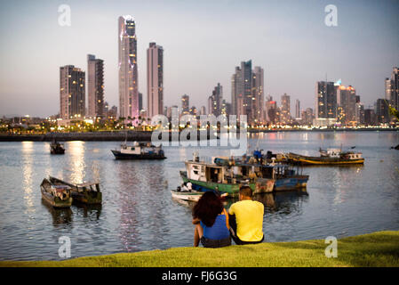 PANAMA-STADT, Panama — Ein Paar genießt an einem Sommerabend die Aussicht in Panama-Stadt, Panama, mit den modernen Wolkenkratzern von Punta Paitilla, die im Hintergrund eine Stadtlandschaft bilden, mit den traditionellen Holzfischbooten von Panama-Stadt im Vordergrund. Am Ufer von Panama City, Panama, an der Panama Bay. Stockfoto