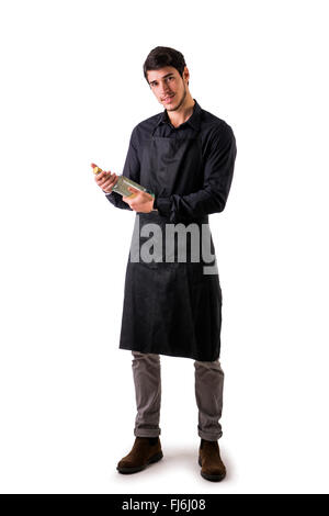 Jungkoch oder Kellner posieren, tragen schwarze Schürze und Hemd isoliert auf weißem Hintergrund, Flasche Wein, die er in der Hand zu betrachten Stockfoto