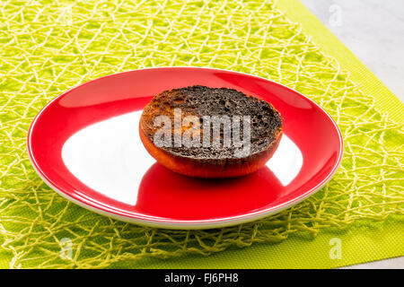 verbranntem Toast, Scheibe, da der Toast schwarz, ruiniert, ungenießbar, Kohle, auf die rote Platte, grüner Hintergrund, Frühling, Frühstück verbrannt ist, Stockfoto