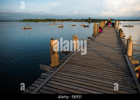 U-Bein-Brücke Taungthaman-See Amarapura Myanmar | AMARAPURA, Myanmar — Die U-Bein-Brücke erstreckt sich im späten Nachmittagslicht über die ruhigen Gewässer des Taungthaman-Sees, ihre lange Reihe von Teakpfählen und Fußgängern erstreckt sich in Richtung des fernen Ufers. Sie wurde etwa 1849-1851 unter König Pagan erbaut und die 1,2-Kilometer-(3.967-Fuß-)Spanne wurde aus Holz gebaut, das beim Abbau der königlichen Gebäude von Inwa gerettet wurde. Kleine Holzboote treiben in der Nähe der Brücke, ein üblicher Anblick, während Fischer und Fährmänner auf dem flachen See arbeiten. Stockfoto