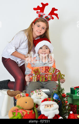 Junge Mädchen und Jungen mit einem Schild Frohe Weihnachten - vor weißem Hintergrund. Stockfoto