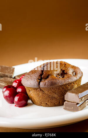 Schoko-Muffin mit Sauerkirschen auf weißen Teller und goldbraun Hintergrund. Textfreiraum Stockfoto