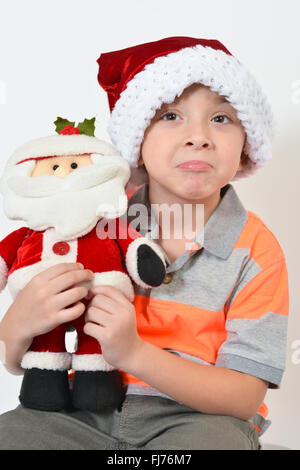 Entzückende junge hält eine Weihnachtsmann Spielzeug während des Tragens einer Weihnachtsmütze - vor weißem Hintergrund. Stockfoto