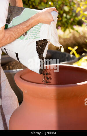 A man einen Garten einen Tontopf vorbereiten, indem man ein Loch und stützen im Boden, dann ausfüllen und Bepflanzung mit Garten-Boden Stockfoto