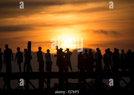 U-Bein-Brücke Teakholz Sonnenuntergang Silhouetten Amarapura Myanmar | AMARAPURA, Myanmar — Menschenmassen verschmelzen zu einem einzigen dunklen Fries vor dem verblassenden Himmel auf der U-Bein-Brücke, die Teakpfosten und menschlichen Silhouetten am Taungthaman-See Myanmars meistfotierte Sonnenuntergangsszene bilden. Um 1849-1851 unter König Pagan aus in Inwa geborgenem Teakholz erbaut, gilt die etwa 1,2-Kilometer-(0,75-Meilen-)Spanne als die älteste und längste Teakholz-Fußgängerbrücke der Welt. Stockfoto