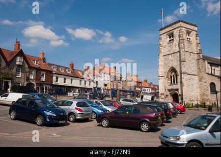 Malton, eine hübsche Stadt, North Yorkshire, England, UK - sonnig, Marktplatz mit alten Kirche, attraktive Geschäfte und Parkplatz, unter blauem Himmel zu vermarkten. Stockfoto