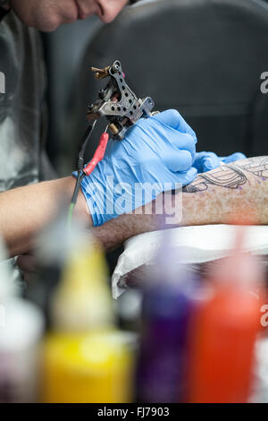 Tattoo-Künstler mit blauen Latex Handschuhen Tätowierungen eine Bio-mechanische Bilder auf Kunden-arm Stockfoto