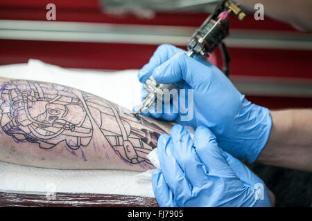 Tattoo-Künstler mit blauen Latex Handschuhen Tätowierungen eine Bio-mechanische Bilder auf Kunden-arm Stockfoto