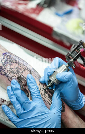 Tattoo-Künstler mit blauen Latex Handschuhen Tätowierungen eine Bio-mechanische Bilder auf Kunden-arm Stockfoto