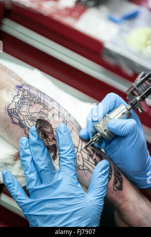 Tattoo-Künstler mit blauen Latex Handschuhen Tätowierungen eine Bio-mechanische Bilder auf Kunden-arm Stockfoto