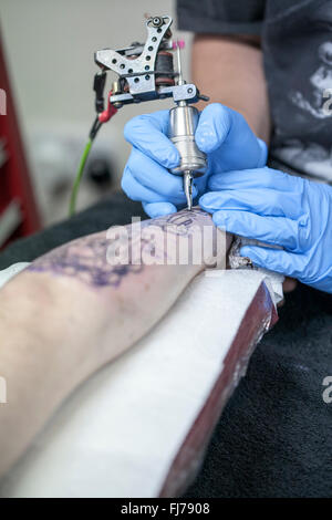 Tattoo-Künstler mit blauen Latex Handschuhen Tätowierungen eine Bio-mechanische Bilder auf Kunden-arm Stockfoto